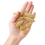 A hand holding a gold embroidered leaf and seed branch applique against a plain white background.