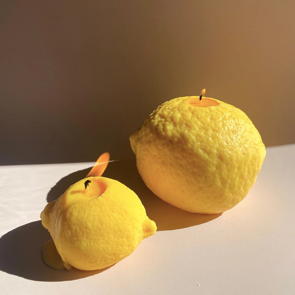 Two lemon-shaped candles on a reflective surface with a warm light source.