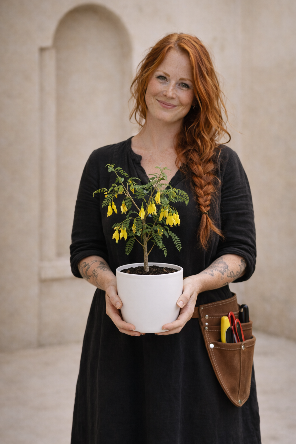 Woman holding a kowhai potted plant with yellow flowers in an outdoor setting