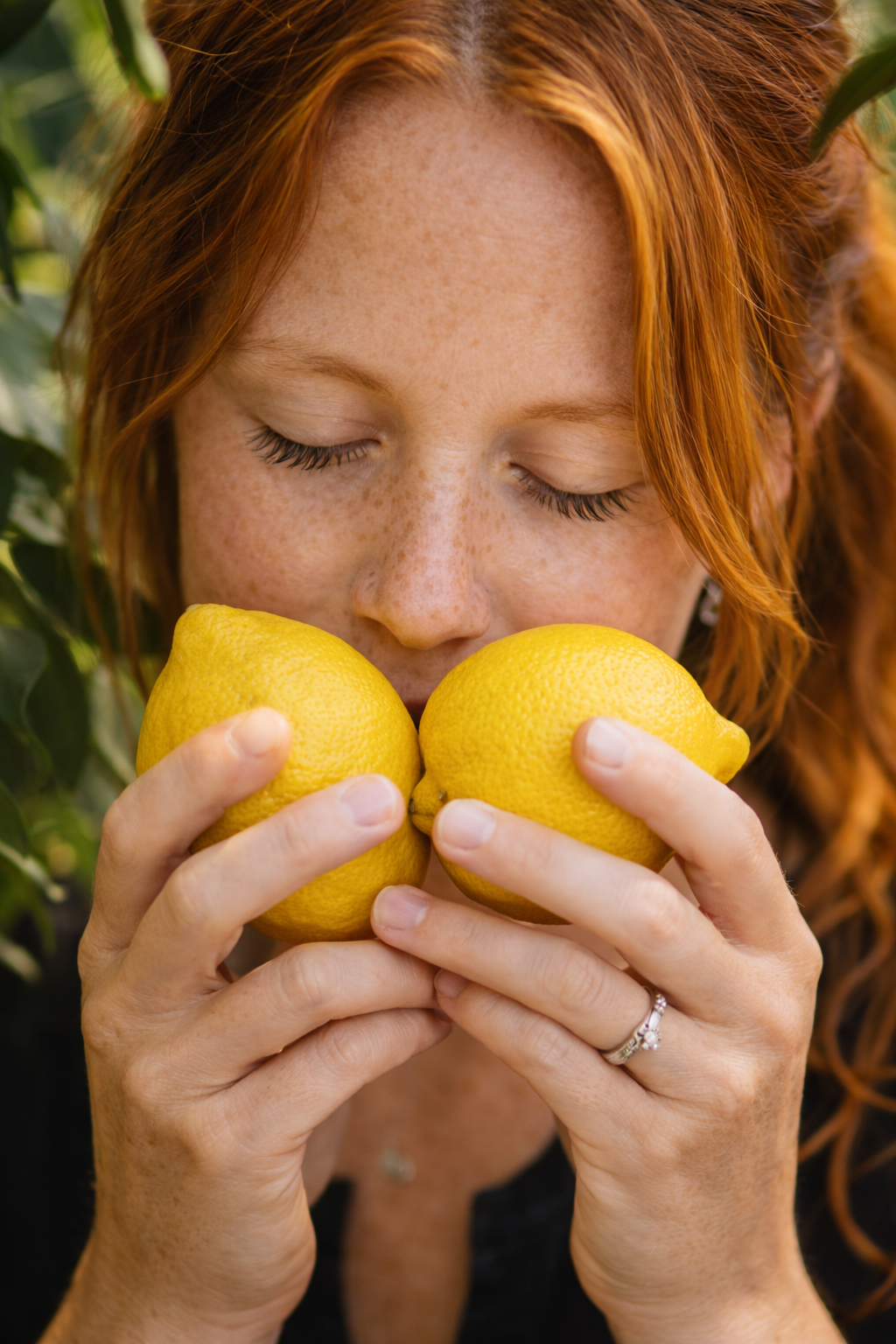 Woman holding two lemons close to her face with a blurred green background