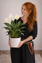 Woman holding a potted Peace Lily plant with white flowers indoors
