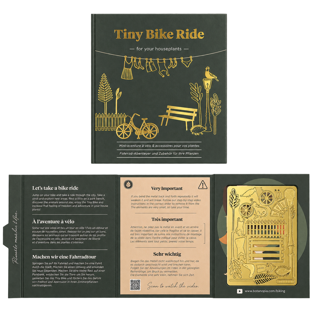 A boxed craft kit titled 'Tiny Bike Ride' shown open to reveal printed instructions, a small bicycle-themed card, and a gold-colored metal component inside a dark olive-green box.