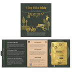 A boxed craft kit titled 'Tiny Bike Ride' shown open to reveal printed instructions, a small bicycle-themed card, and a gold-colored metal component inside a dark olive-green box.